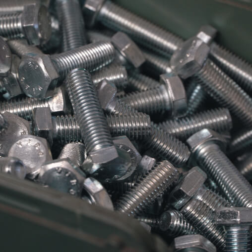 Primo piano di un contenitore metallico pieno di bulloni esagonali in acciaio zincato di varie misure.