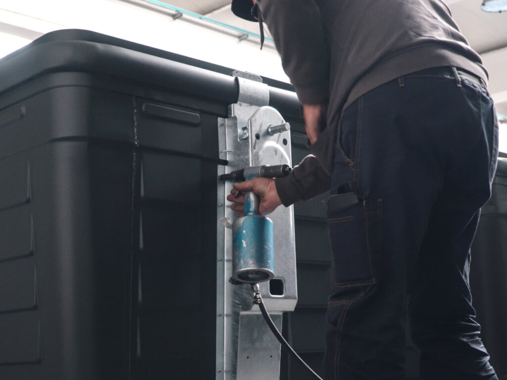 Tecnico che esegue l'assemblaggio e il serraggio di componenti meccanici su un cassonetto nero, utilizzando un avvitatore pneumatico in un'officina.