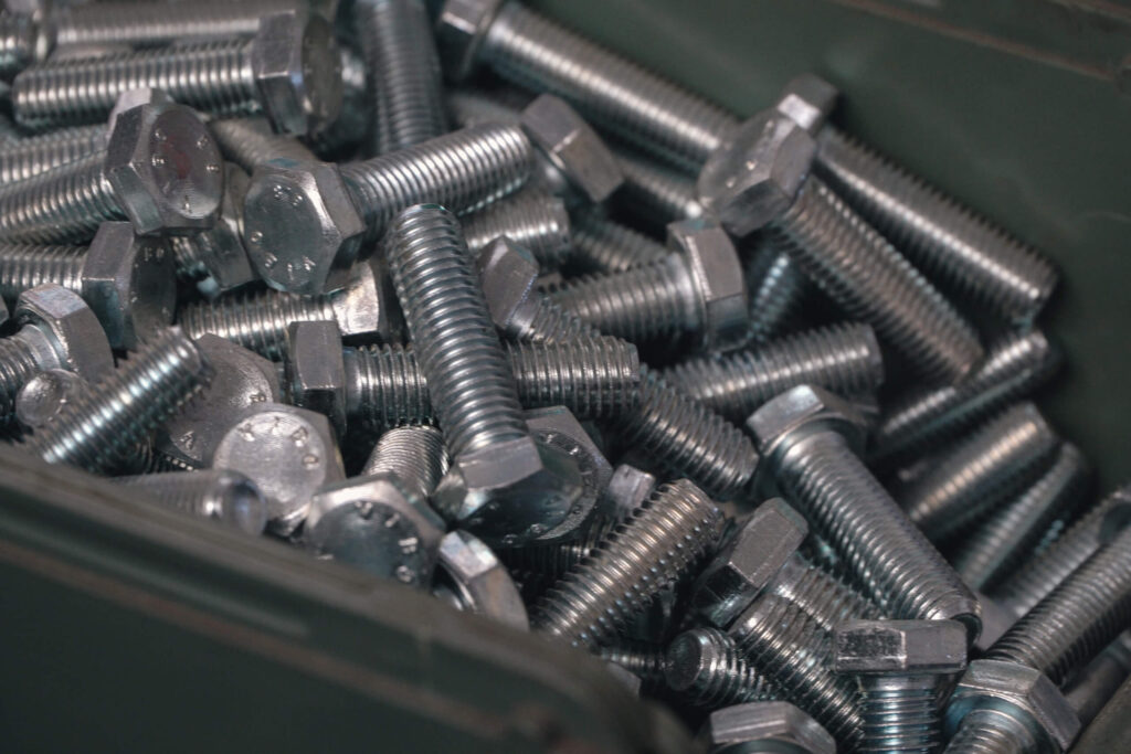 Primo piano di un contenitore metallico pieno di bulloni esagonali in acciaio zincato di varie misure.